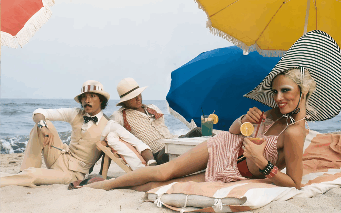 Photo of Antonio Lopez, Corey Tippin, and Donna Jordan, St.-Tropez, 1970 laying on the sand with drinks and beach umbrella