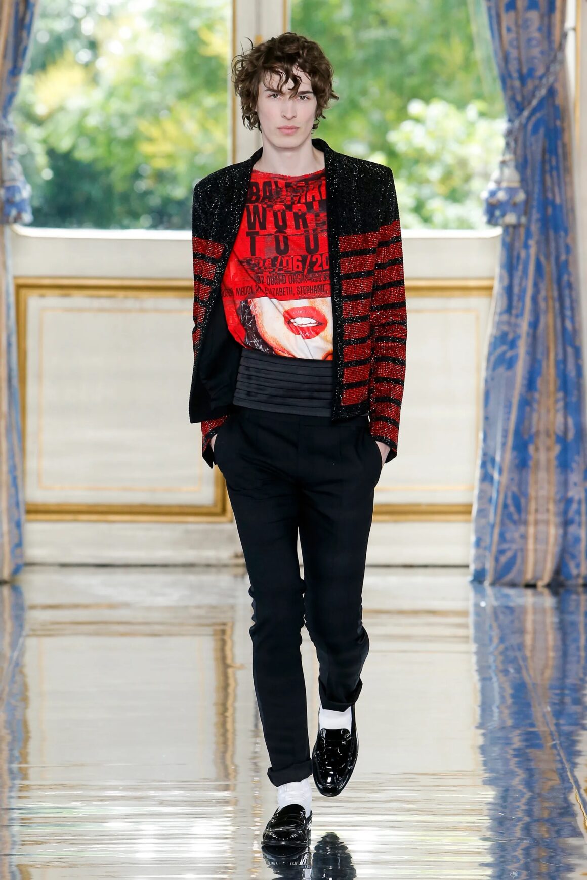 Male model wearing black and red graphic tee with a black and red stripe jacket, black pants, black shoes, and white socks