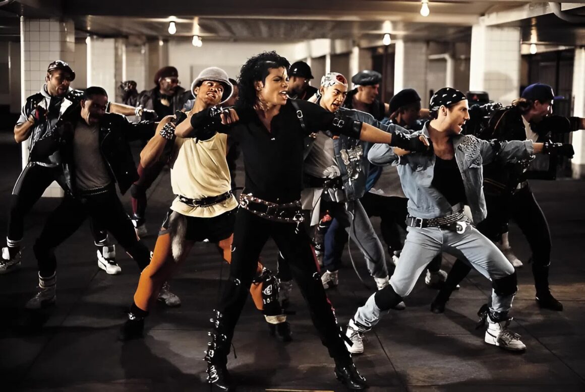 Michael Jackson wears black clothing and gloves and is surrounded by male dancers